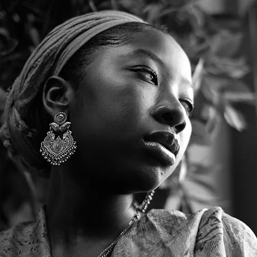 A woman with a gold earring and hairband, her head tilted to the side. 