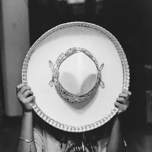 A women covering her face with an ornate white sombrero. 